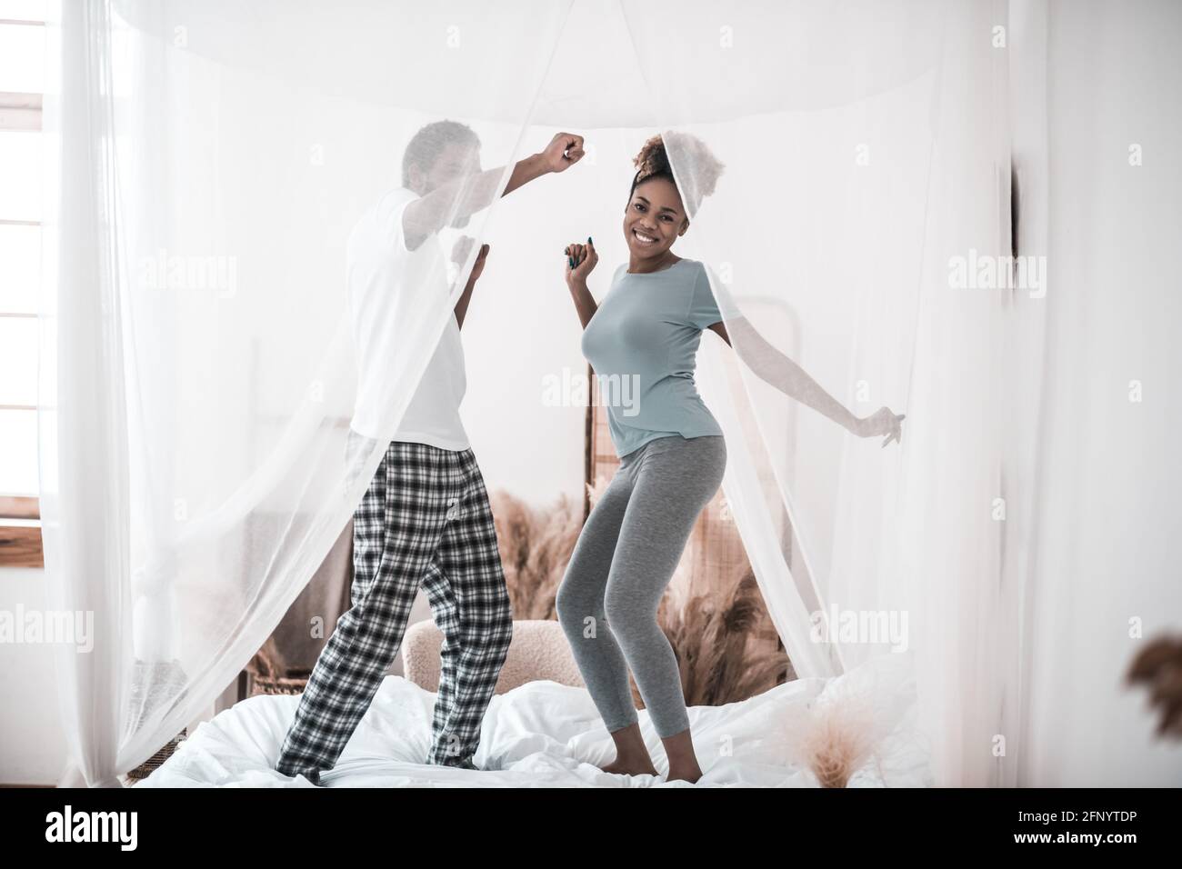 Fröhlicher Mann und Frau im Schlafanzug, die auf dem Bett tanzen Stockfoto