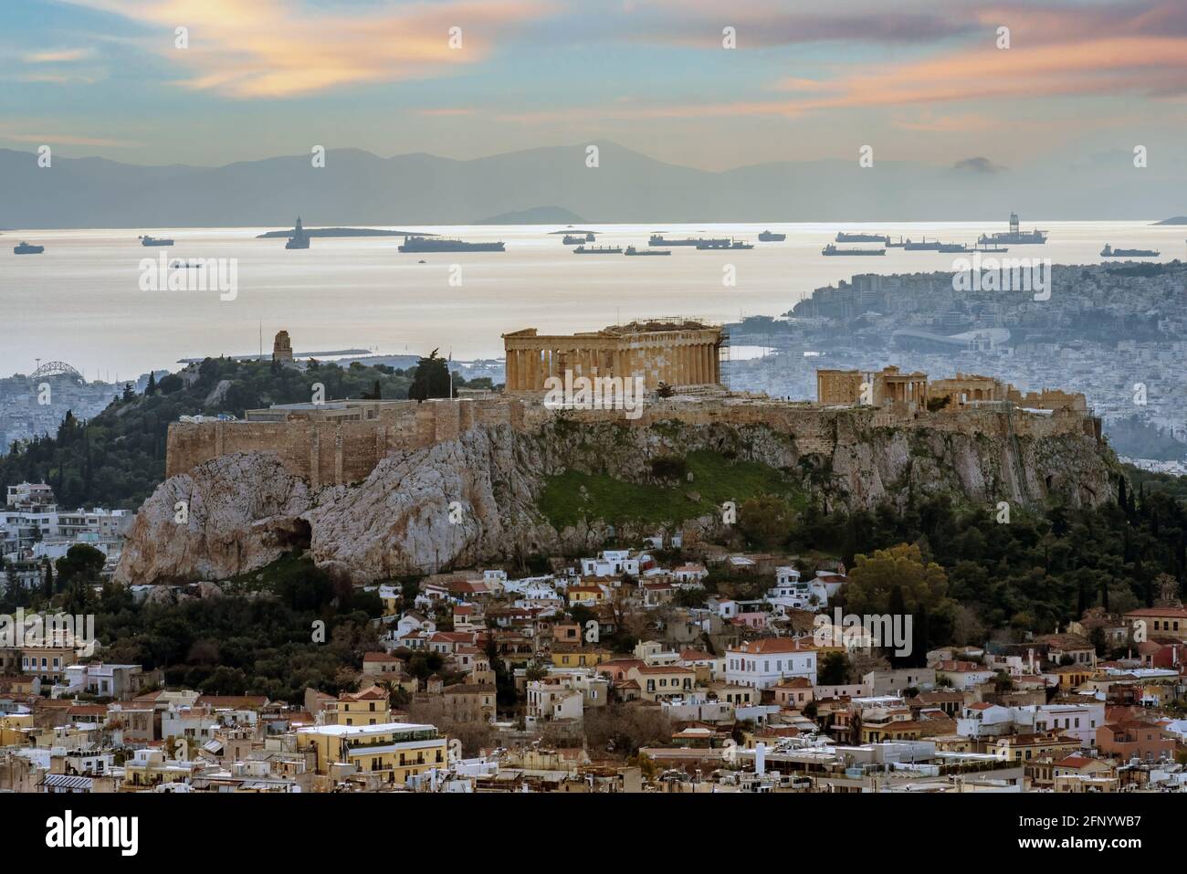 Die Akropolis von Athen mit Parthenon-Tempel vom Lycabettus-Hügel aus gesehen. Plaka-Viertel unter der Akropolis. Schiffe vertäuten vor dem Hafen von Piräus. Sonnenuntergang Stockfoto