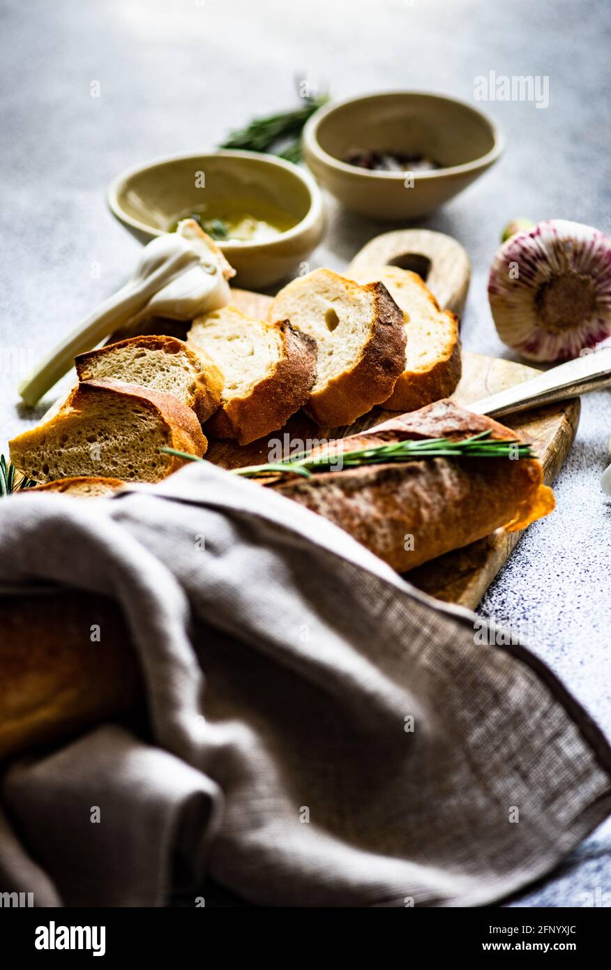 Geschnittener Baguette-Laib mit einer Schüssel Olivenöl, Knoblauch, Salz, Pfeffer und Rosmarin Stockfoto