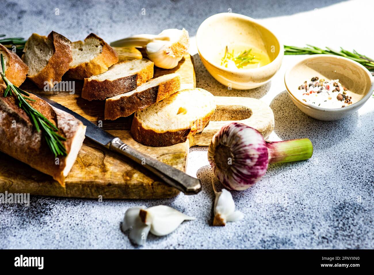 Geschnittener Baguette-Laib mit einer Schüssel Olivenöl, Knoblauch, Salz, Pfeffer und Rosmarin Stockfoto