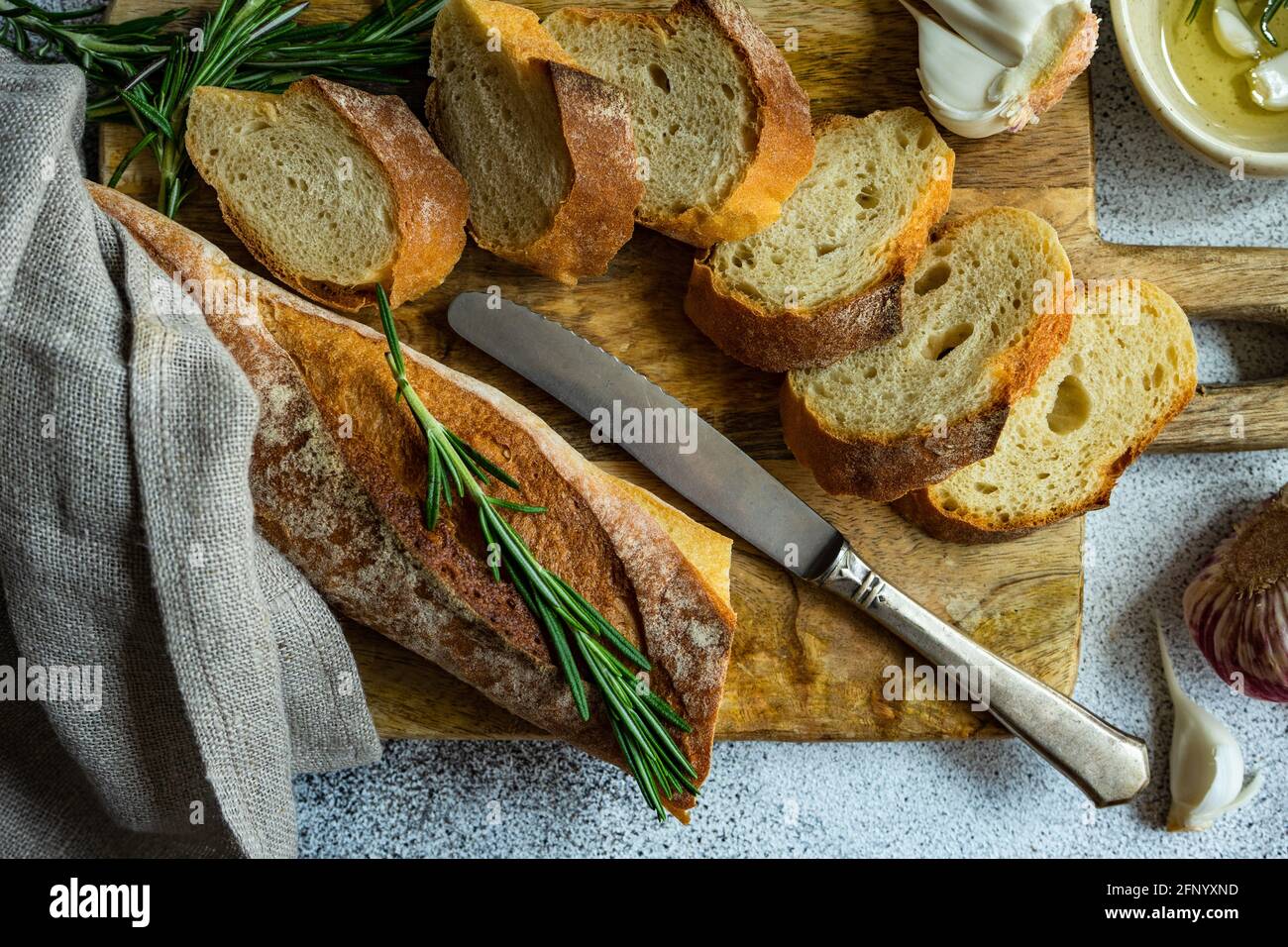 Blick von oben auf den in Scheiben geschnittenen Baguette-Laib mit einer Schüssel Olivenöl, Knoblauch und Rosmarin Stockfoto