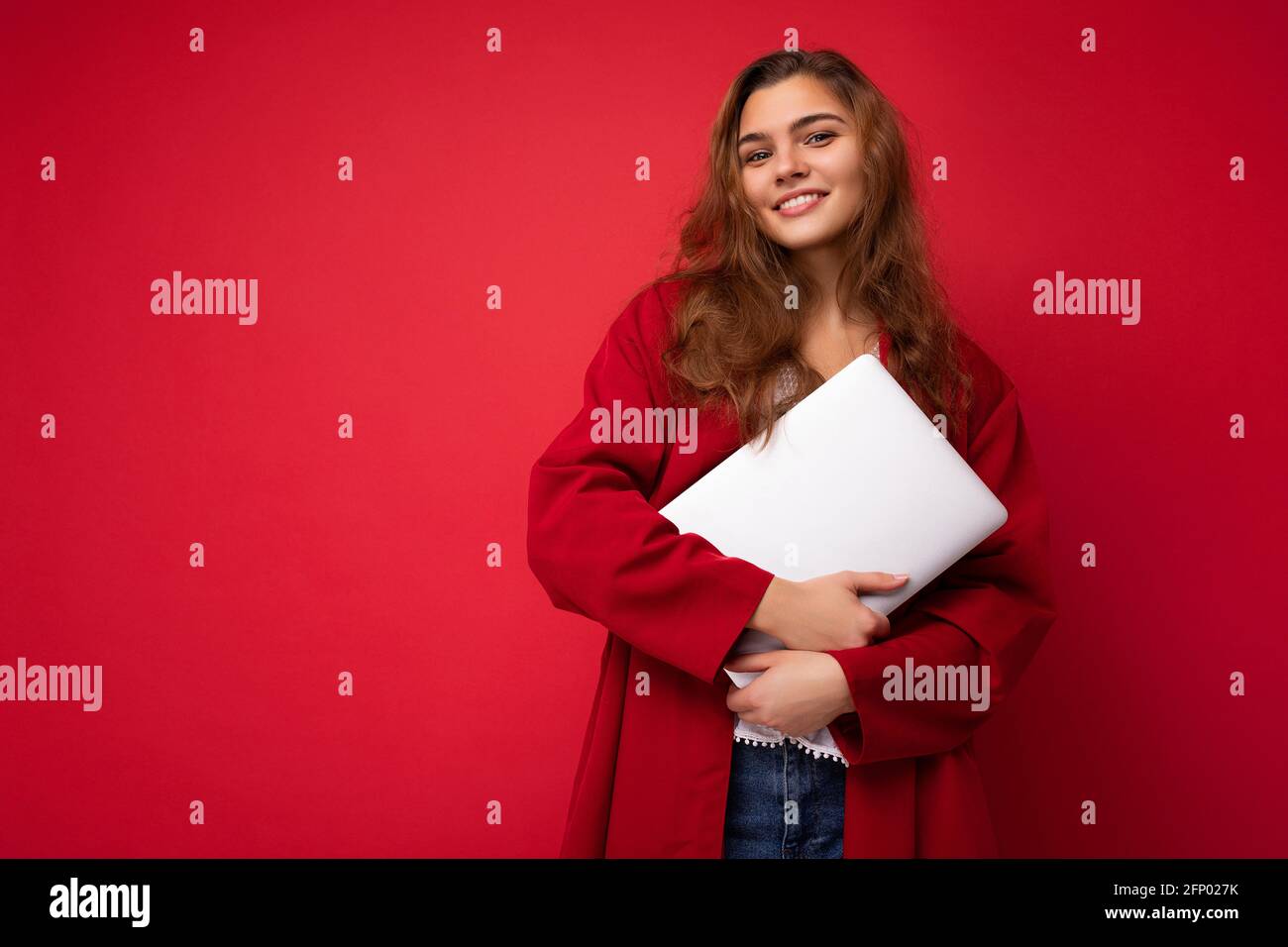 Nahaufnahme Porträt einer schönen lächelnden jungen Brünette Frau mit Netbook-Computer Blick auf die Kamera trägt rote Strickjacke isoliert an der roten Wand Stockfoto