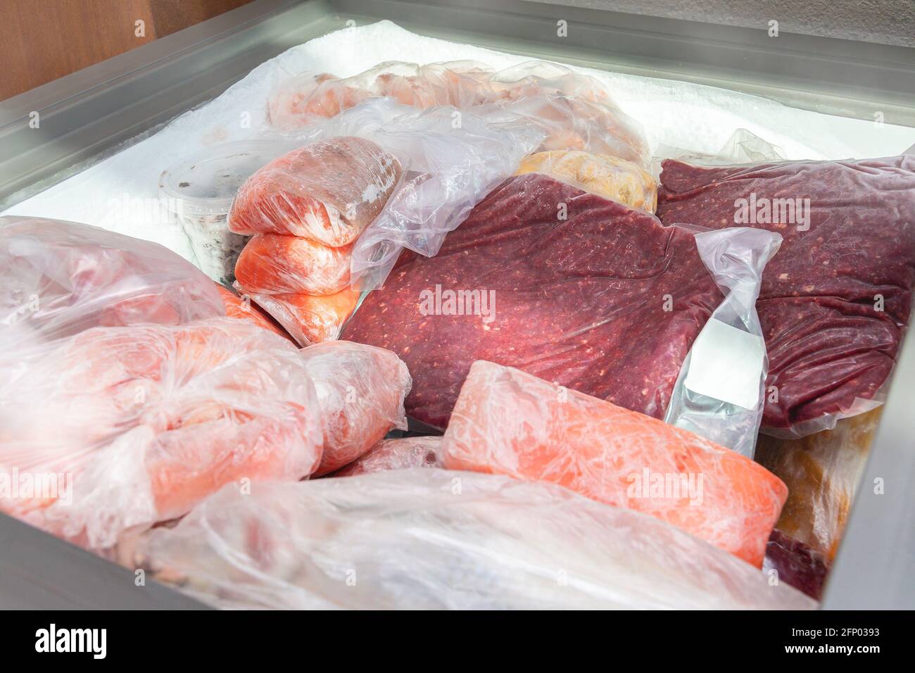 Tiefkühlkost im Gefrierschrank. Tiefgekühltes Fleisch und andere Lebensmittel in einem horizontalen Gefrierschrank verpackt. Lebensmittelkonservierung bei niedrigen Temperaturen. Stockfoto