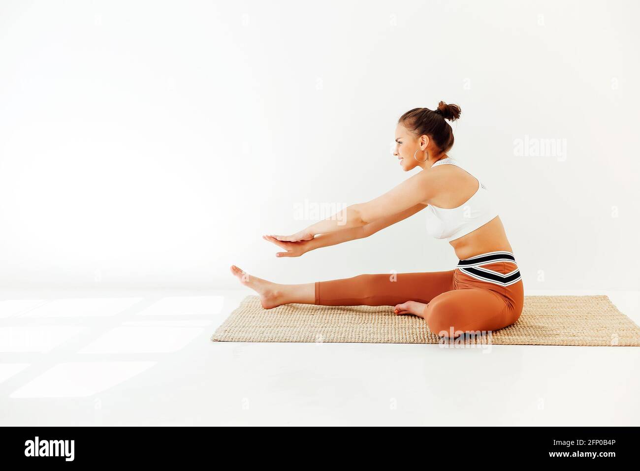 Junge Brünette weiblich in Sportkleidung sitzt auf der Matte und macht Yoga, während Achtsamkeit üben. Konzept der physischen und psychischen Gesundheit Stockfoto