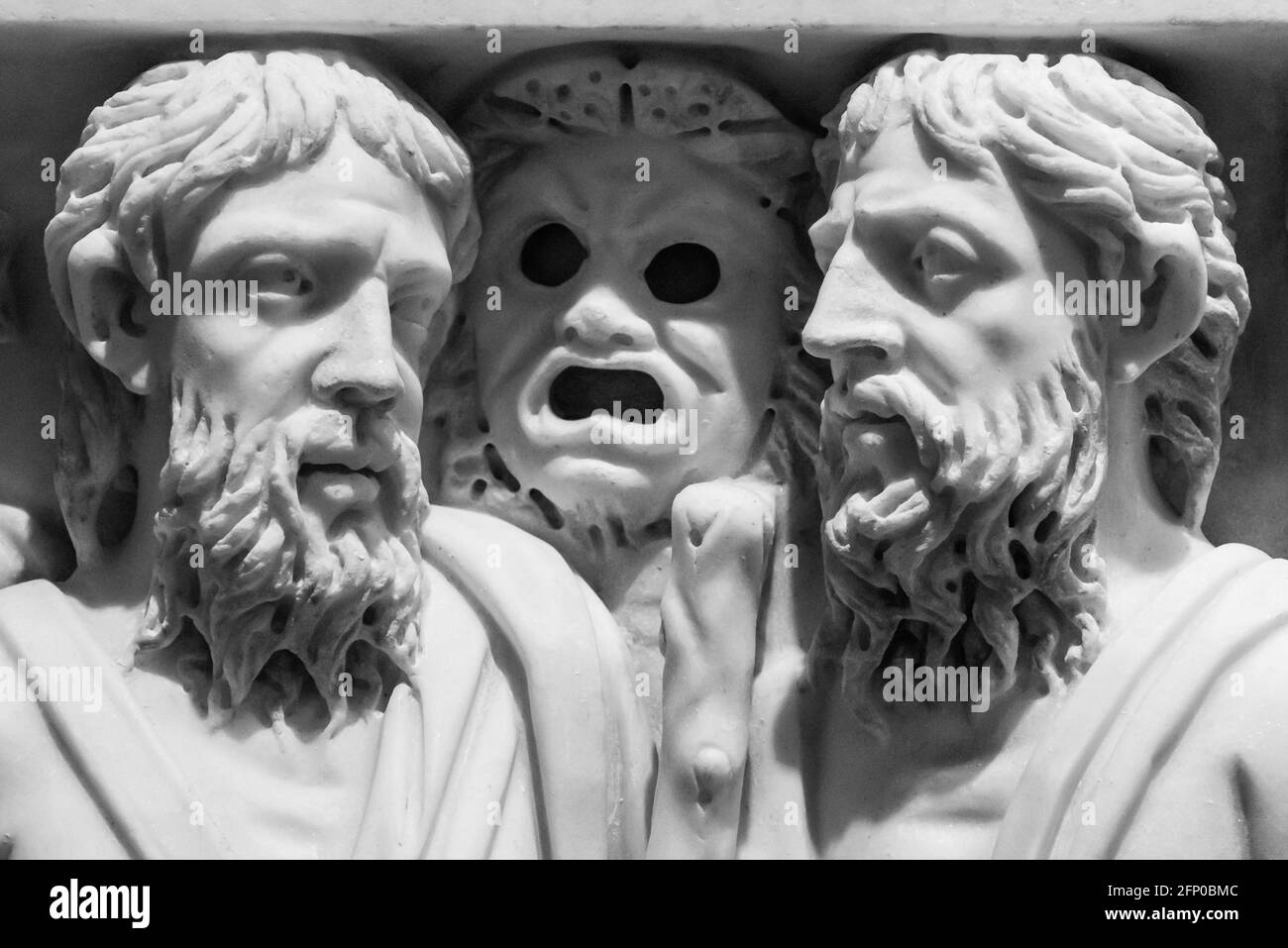 Schwarz-Weiß-Foto von alten römischen Skulpturen geschnitzt auf Eine Marmorwand, an der zwei bärtige Männer im Detail sprechen Und eine gruselige Maske zwischen ihnen Stockfoto