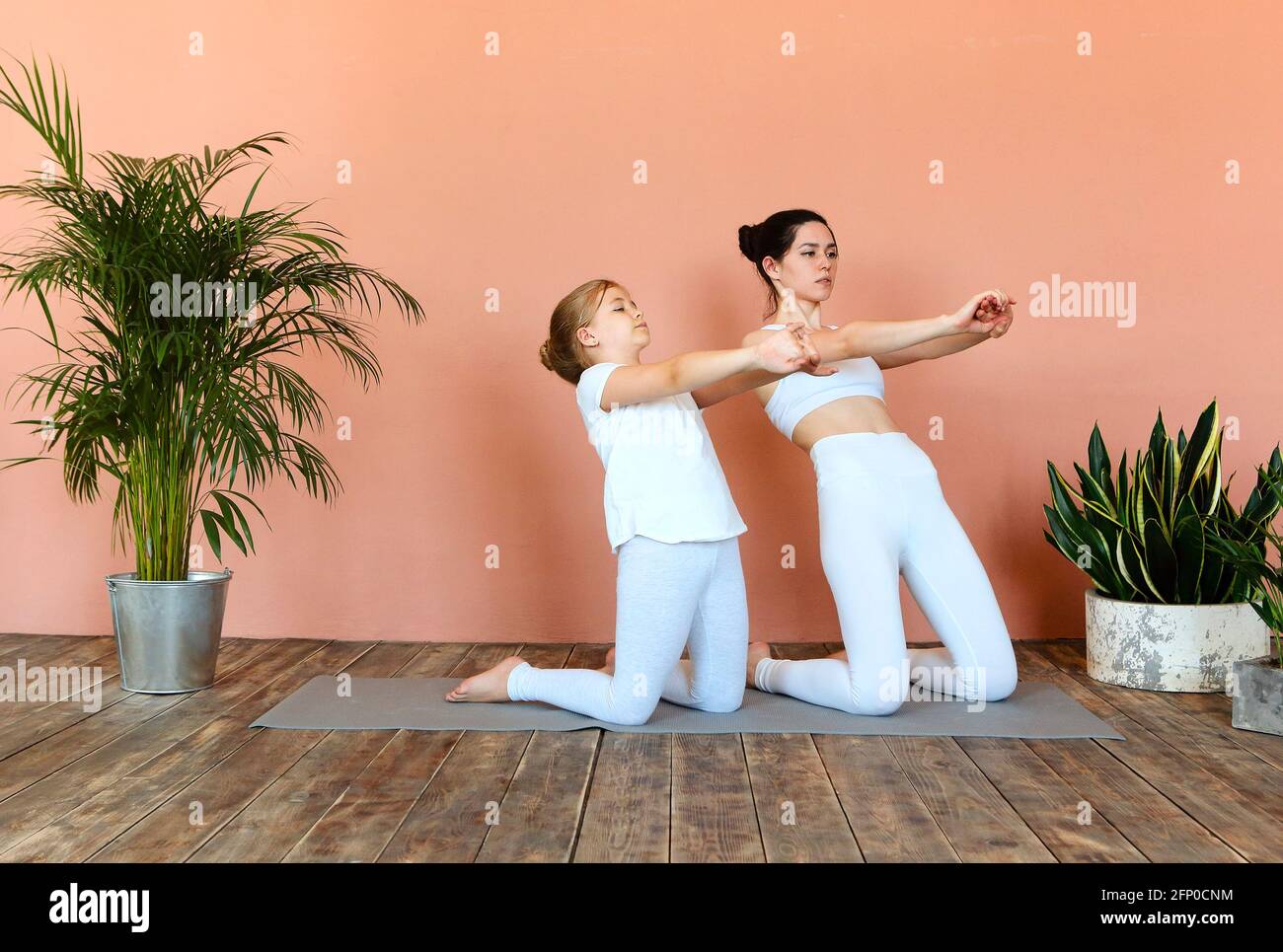 Seitenansicht einer lächelnden Frau und eines kleinen Mädchens, die Yoga praktizieren Beim Stehen auf der Matte im gemütlichen Wohnzimmer und Wegschauen Stockfoto