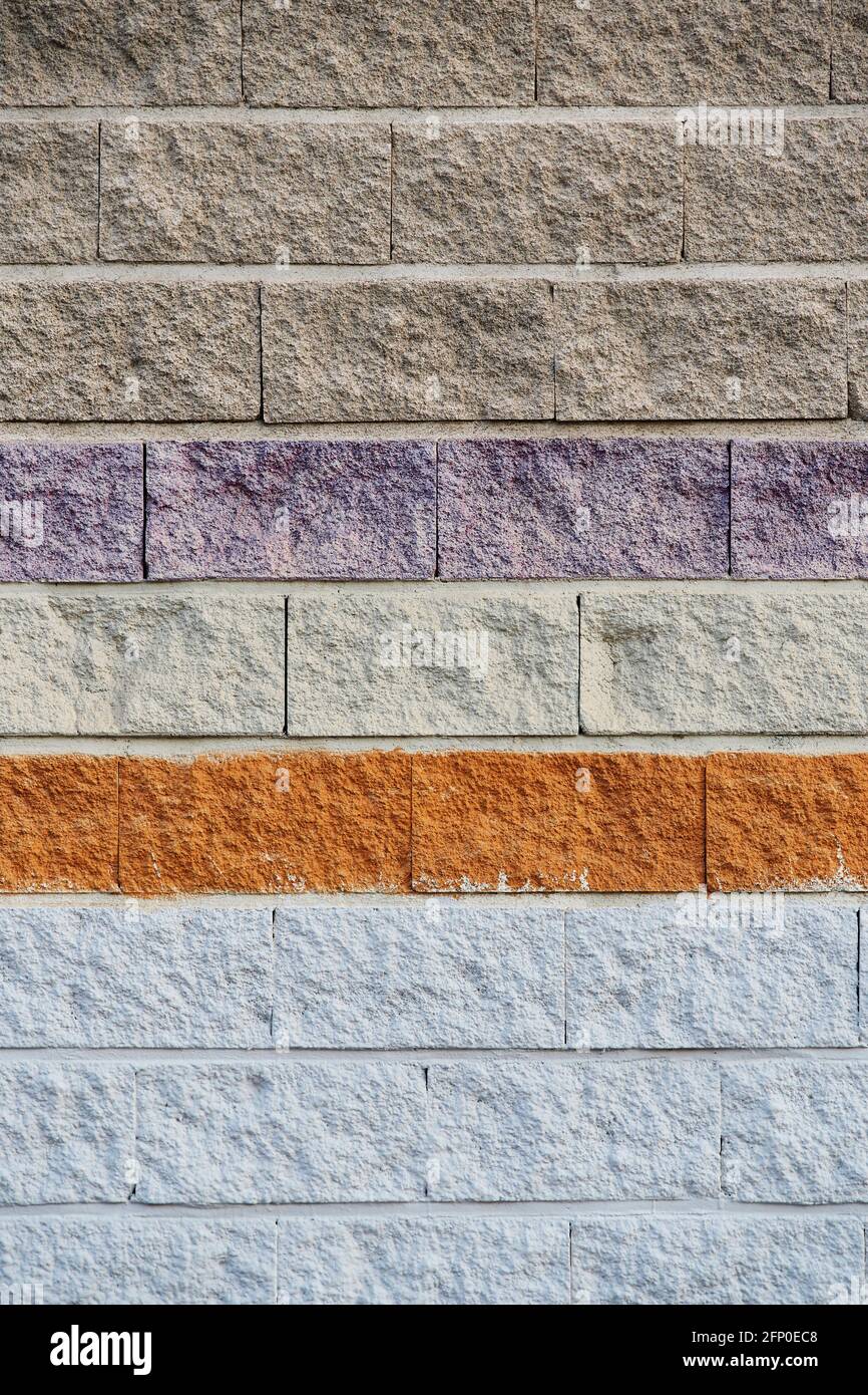 Vertikale Aufnahme einer rauen Betonblockwand mit grauen, violetten und roten Farben. Stockfoto