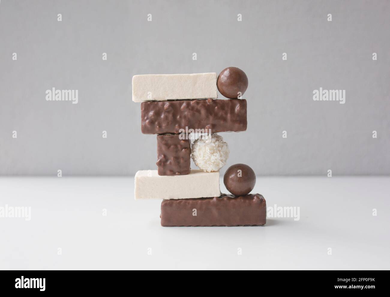 Bonbons, Sumpflaibe und Waffeln auf weißem Hintergrund vor grauer Wand angeordnet. Kunst- und Food-Design-Konzept. Stockfoto