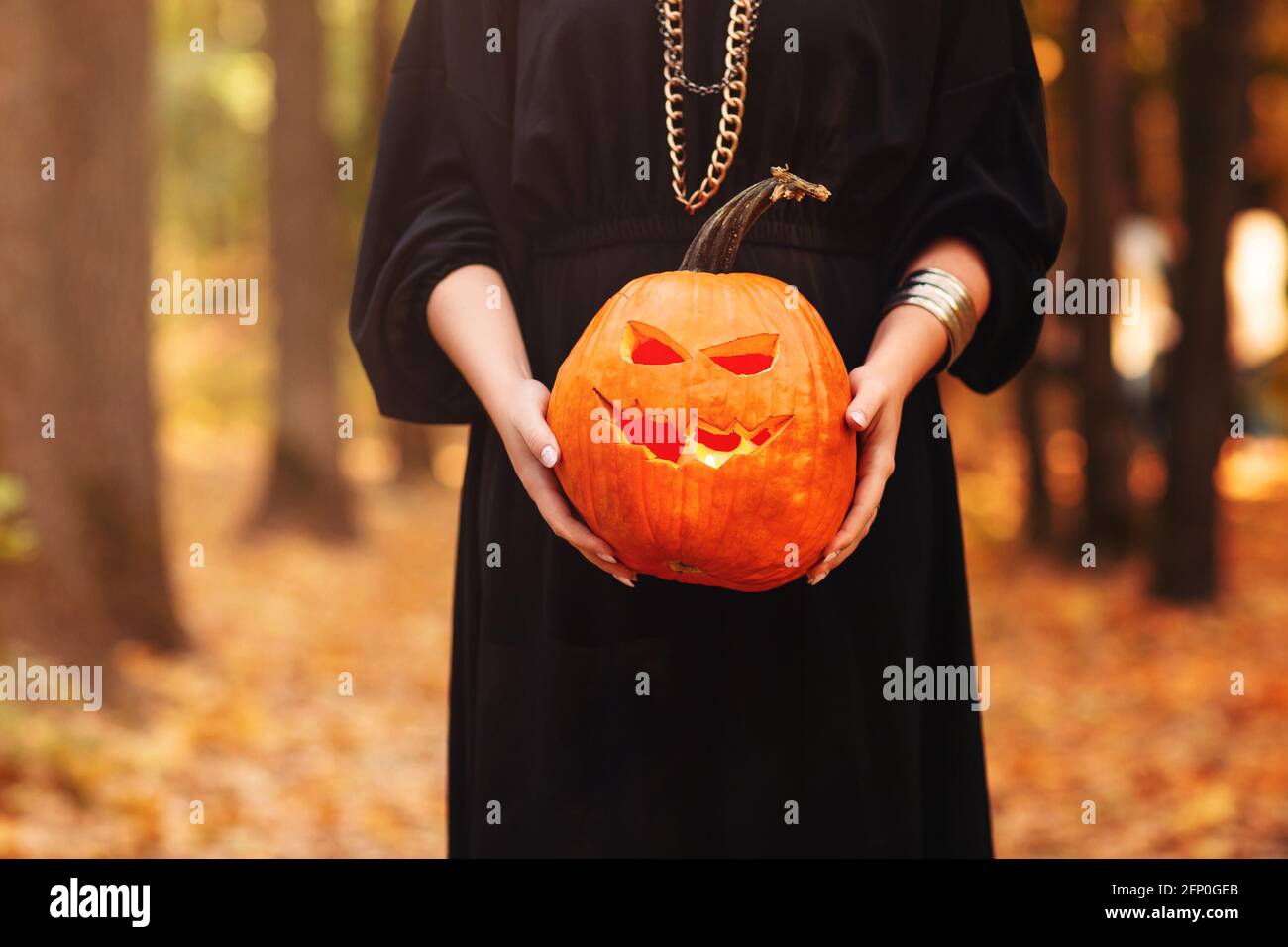 Junge Frau in schwarzem Umhang mit gruseligen Jack o Laterne Und auf den Halloween-Tag im Herbstwald wegschauen Stockfoto