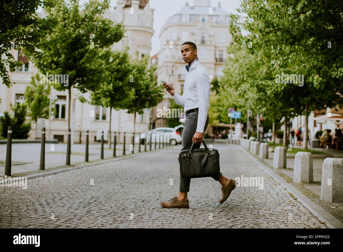 Hübscher junger afroamerikanischer Geschäftsmann, der ein Mobiltelefon benutzt Eine Straße abtreten Stockfoto
