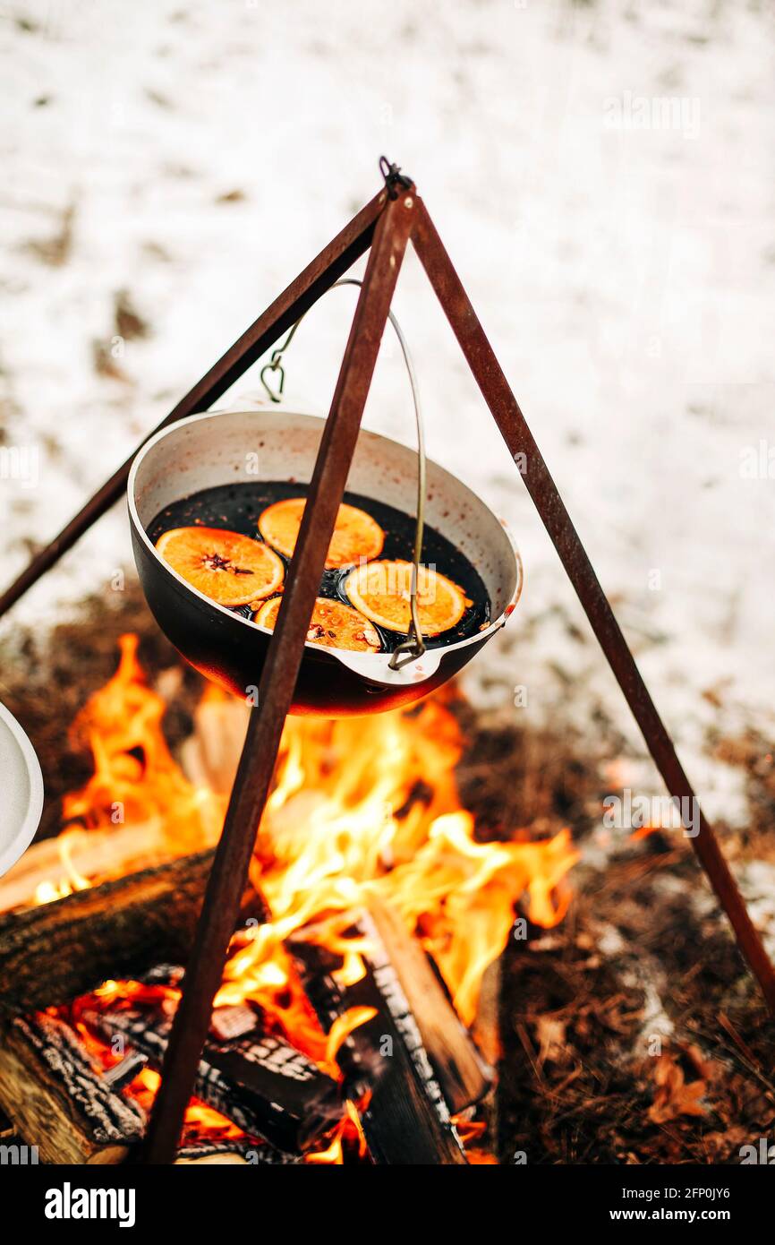 Von oben traditionellen Glühwein mit Scheiben von Orange Vorbereitung Im Topf über brennenden Baumstämmen im Winter auf dem Land Stockfoto