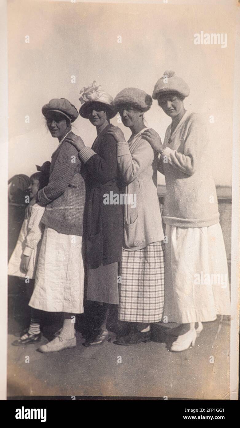 Authentisches Vintage-Foto von 1910 von vier jungen Frauen und einem Kind in Röcken und Hüten, die die Schultern berühren. Konzept der Zweisamkeit, nostalgisch Stockfoto