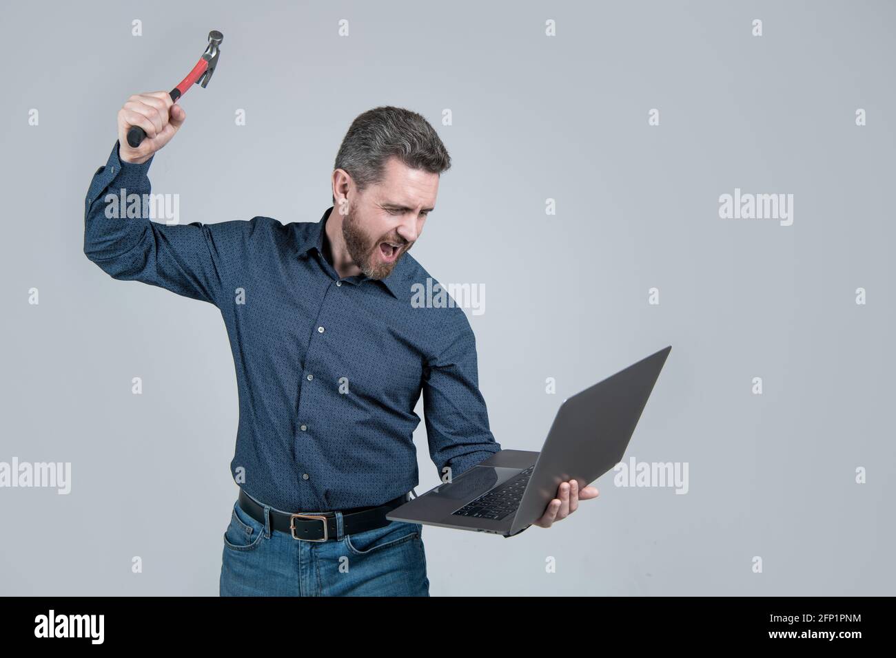 Loslassen von Ärger am Computer. Gestresster Mann schrie und brach Laptop mit Hammer. Wurde gestresst Stockfoto