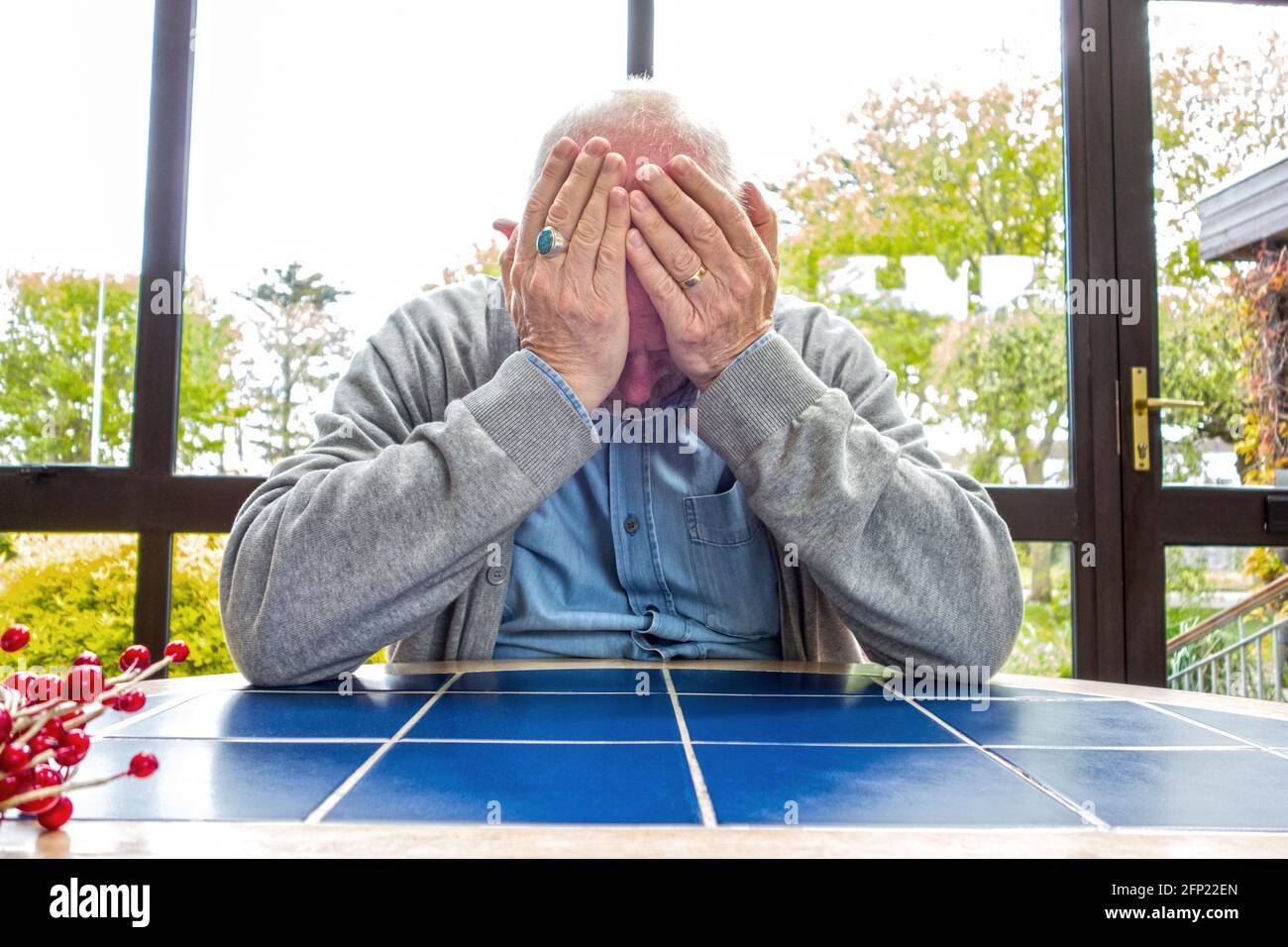 Ein Mann saß an einem Tisch, hielt seinen Kopf in den Händen, beunruhigt, deprimiert, bestürzt Stockfoto