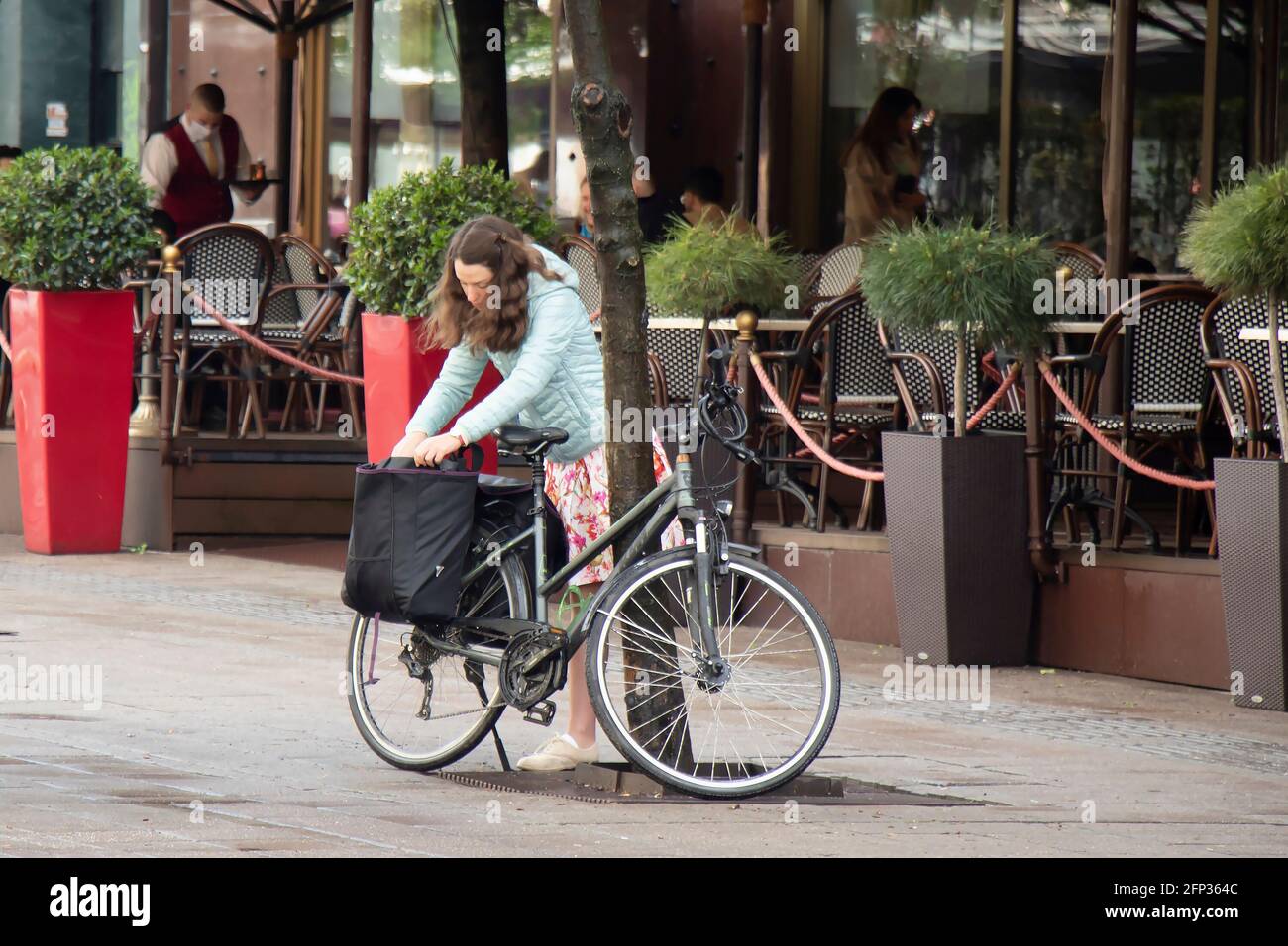 Belgrad, Serbien - 13. Mai 2021: Eine junge Frau packte doppelte Fahrradtaschen auf ihrem geparkten Fahrrad auf einer Straße in der Nähe der Cafeterrasse Stockfoto