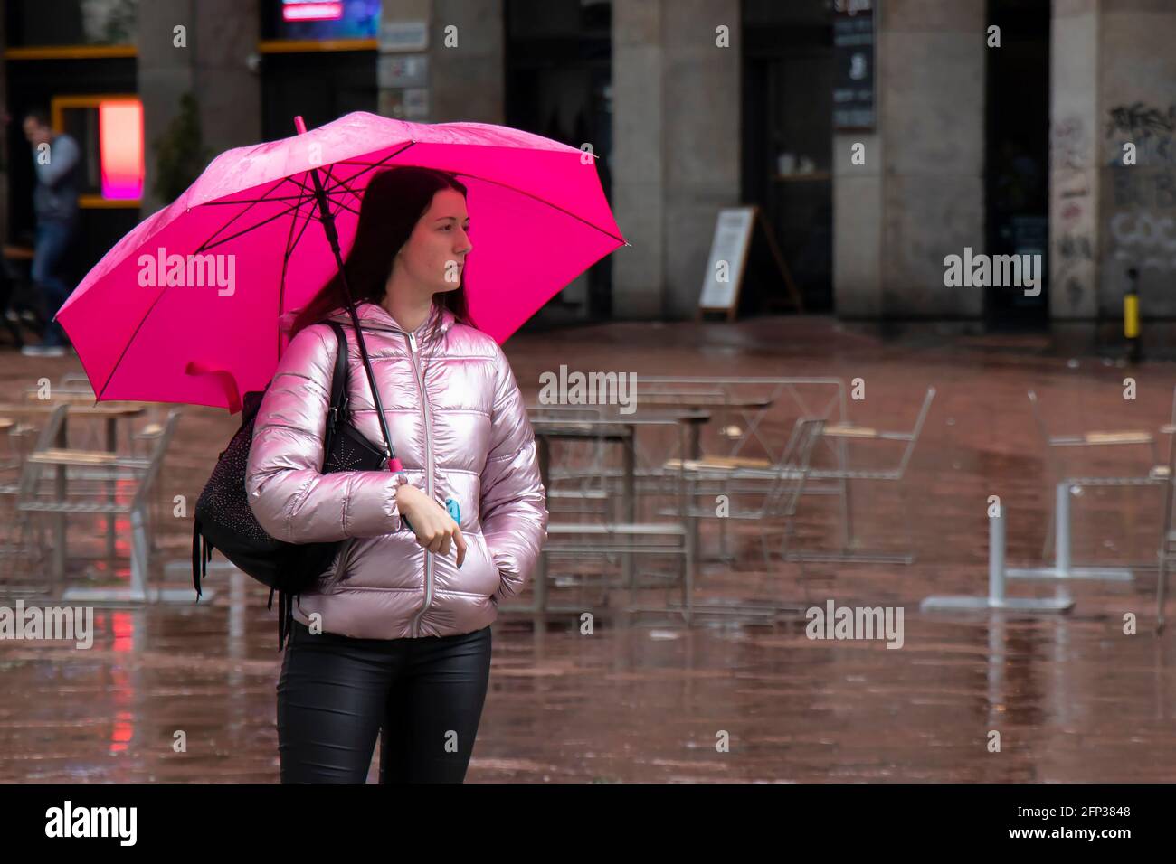Belgrad, Serbien - 13. Mai 2021: Eine junge Frau, die allein unter dem Schirm steht und an einem regnerischen Tag auf dem Stadtplatz wartet Stockfoto