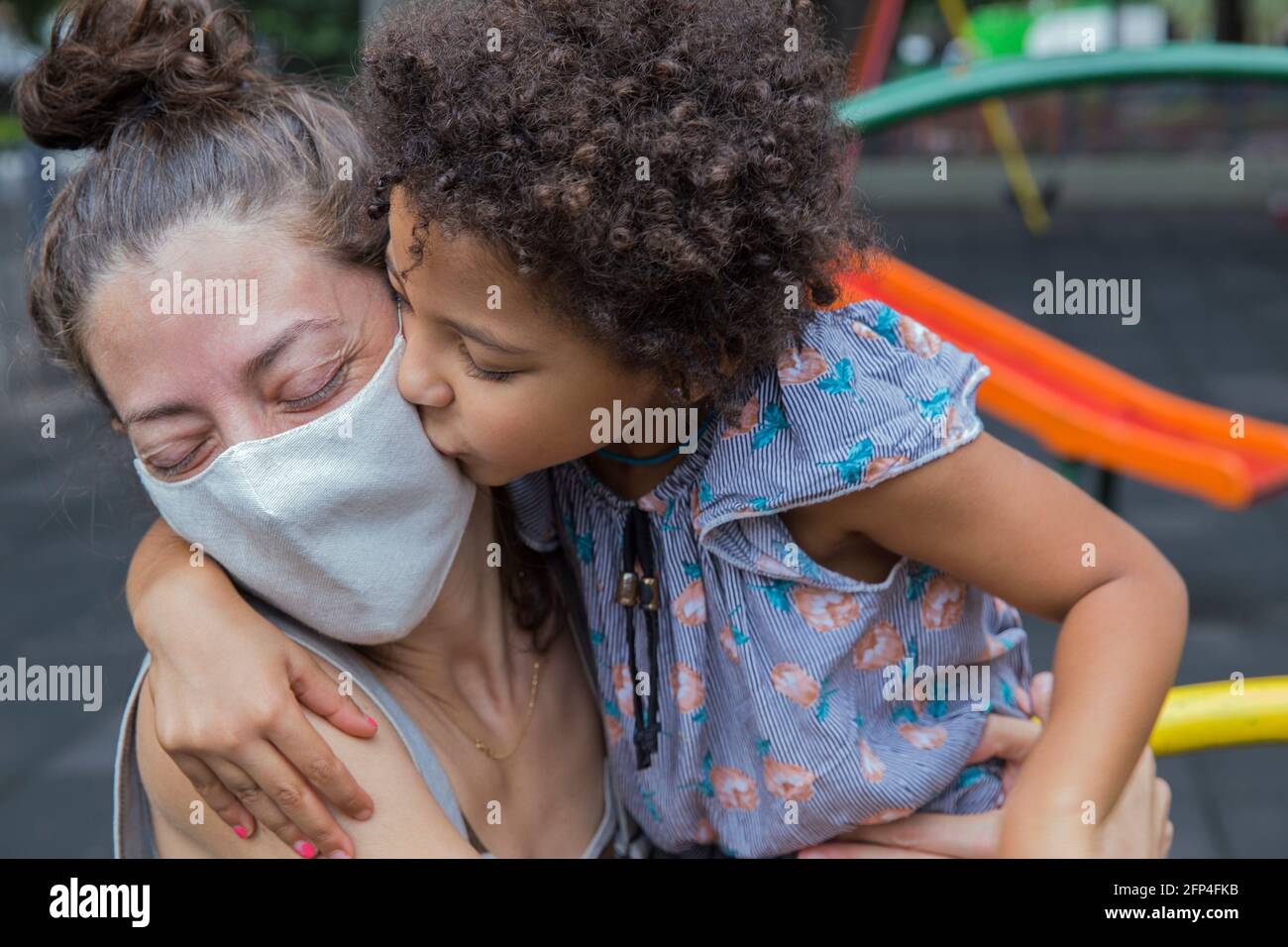 Nettes Mädchen küsst ihre Mutter auf Spielplatz draußen in einem neuen normalen Leben. Stockfoto