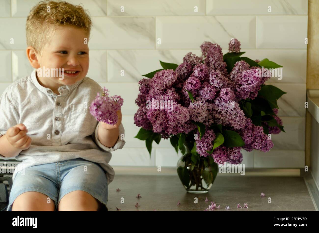 Junge 2 Jahre alt glücklich mit Fliederblüten Stockfoto