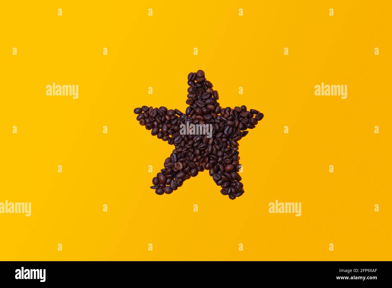 Kaffeebohnen gruppieren sich zusammen und bilden die Figur eines Sterns, der auf einem gelben Hintergrund von oben betrachtet isoliert ist. Es gibt Platz für Text oder Logos. Stockfoto