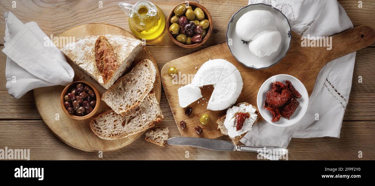 Käseplatte mit Ricotta und Mozzarella scamorza, Brot, getrockneten Tomaten, Oliven und nativem Olivenöl extra auf Holzboden. Italienische Spezialität Stockfoto