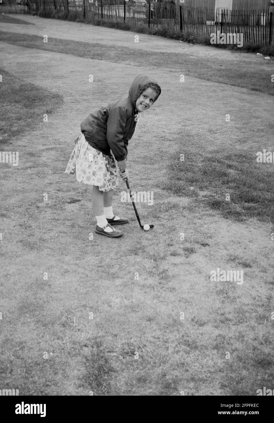 1962, historisch, ein kleines Mädchen in einem Kleid und Anorak, Golf auf einem Putting Course am Meer, Littlehampton, West Sussex, England, Großbritannien. Stockfoto