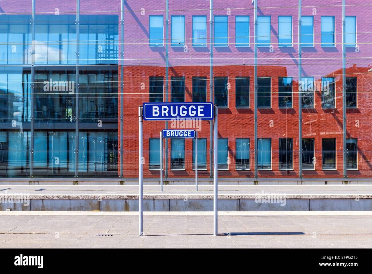 Bahnhof mit Namensschild der Stadt Brügge (Brügge in Femish) auf Plattform im Sommer mit modernem Hauptgebäude, Belgien. Konzentrieren Sie sich auf das Namensschild. Stockfoto