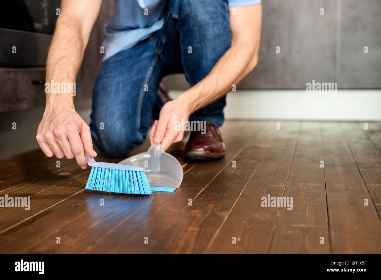 Mann fegen Staub mit Besen auf Dustpan, Housekeeping Concept, Close-Up Photo. Konzentrieren Sie Sich Auf Den Blauen Besen Für Die Reinigung Stockfoto