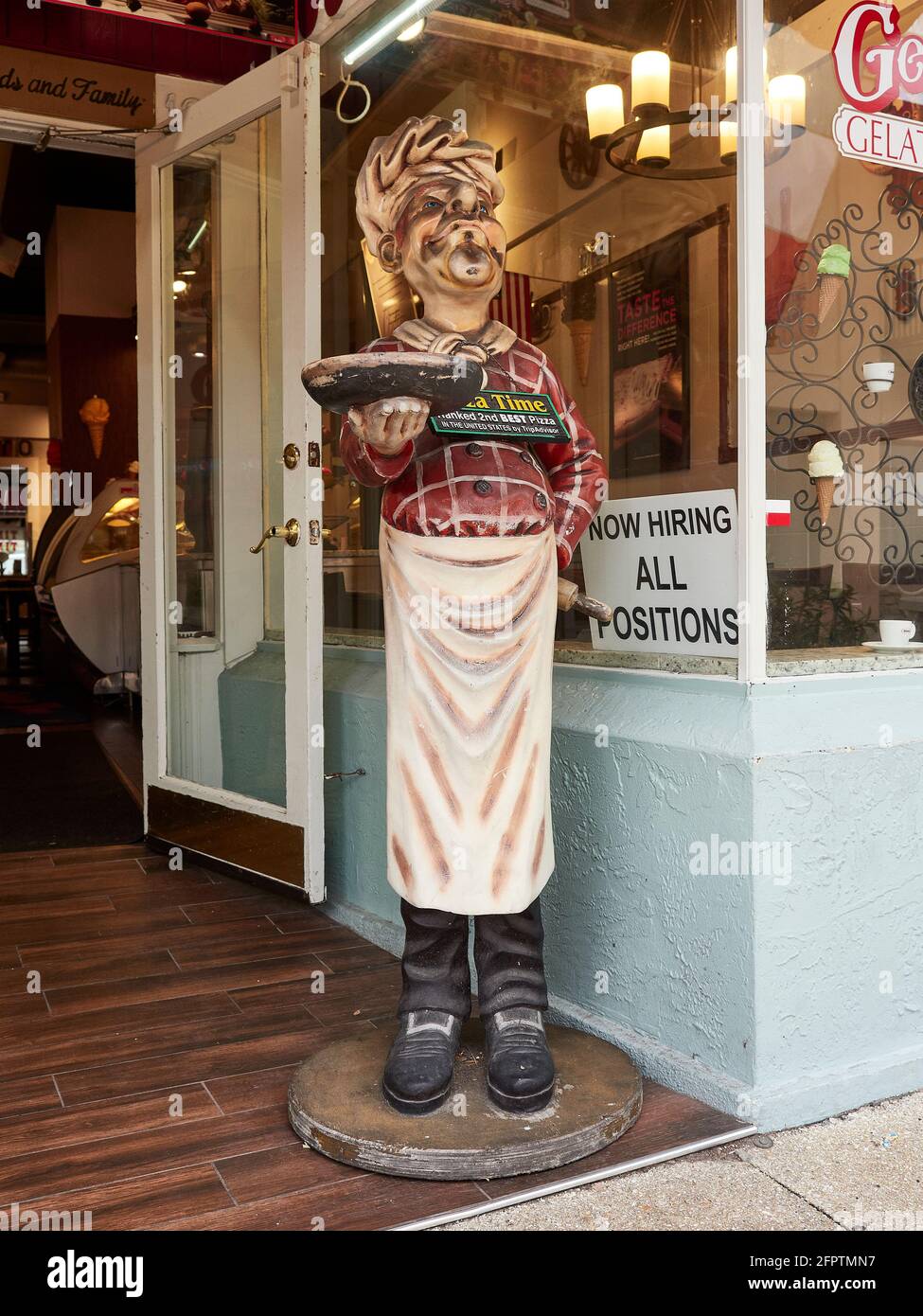 Eine große Statue oder Figur des Küchenchefs vor einem Pizzalestaurant, die eine Pizza mit einem Schild mit Hilfswünschen im Fenster in St. Augustine, Florida, USA, hält. Stockfoto
