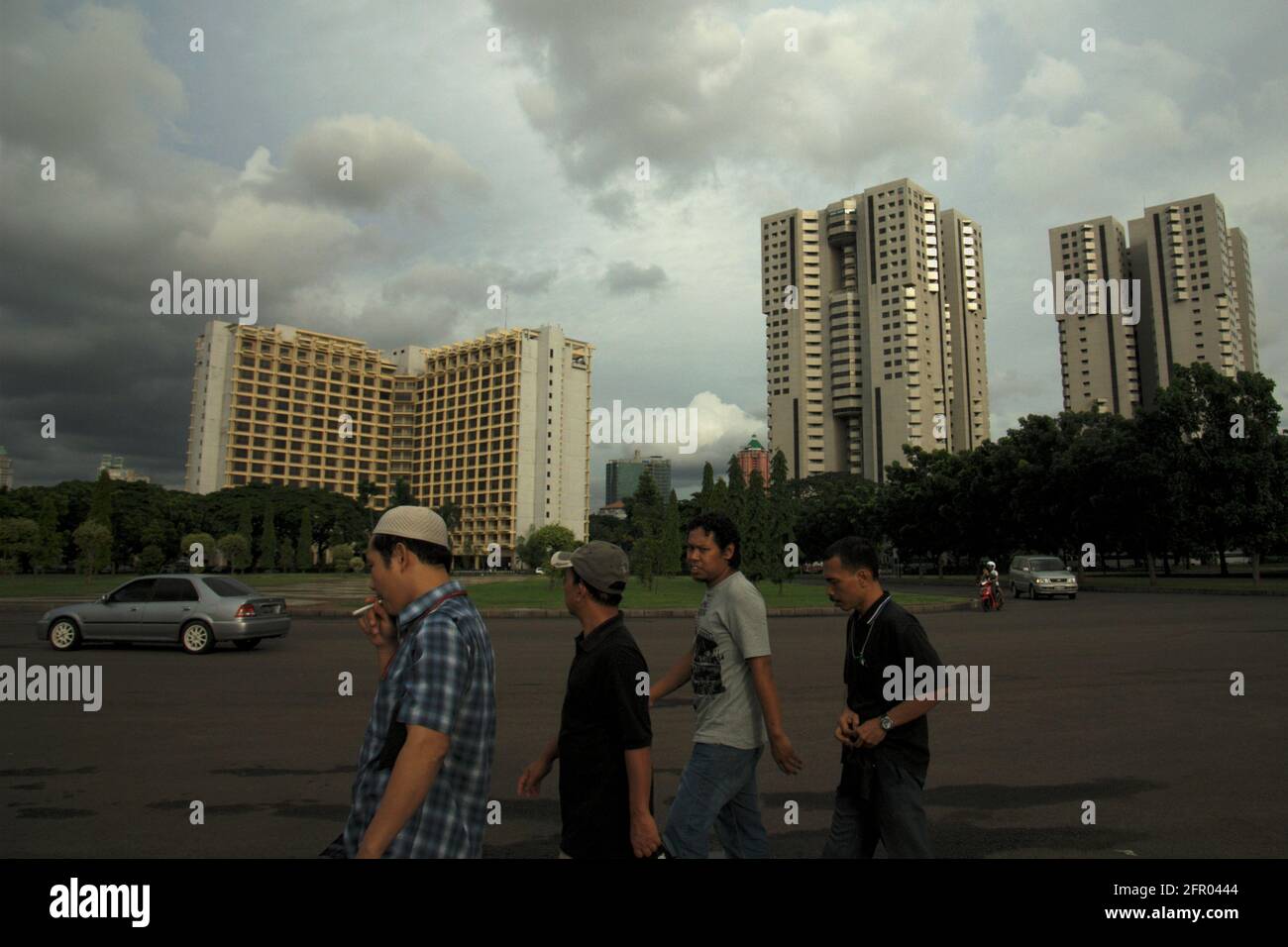 Eine Gruppe von Männern, die die Straße entlang um den East Park in Gelora Bung Karno (Senayan Sports Complex) mit einigen hoch aufragenden Gebäuden gehen, kann in der Ferne gesehen werden. Jakarta, Indonesien. Stockfoto