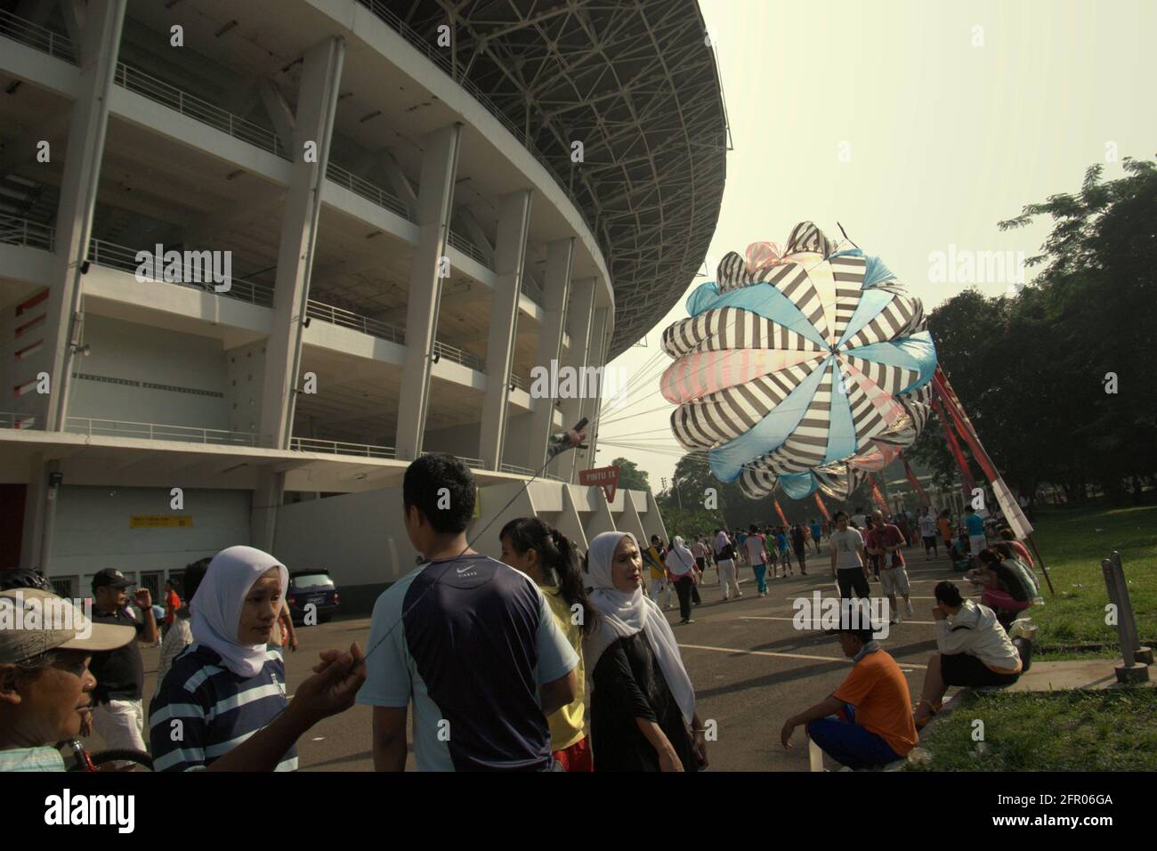 Wanderin von Kindern, die Fallschirm spielen, der zwischen Menschen mit Freizeitaktivitäten vor dem Senayan Main Stadium (Gelora Bung Karno Stadium) in Jakarta, Indonesien, arbeitet. Stockfoto