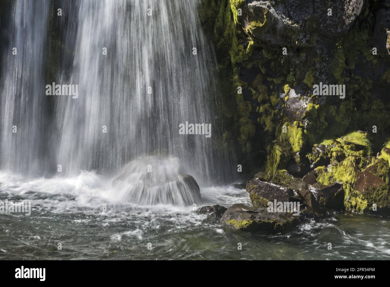 Long Exposure Wasserfall mit Felsen, die mit grünem Moos bedeckt sind. Island Stockfoto