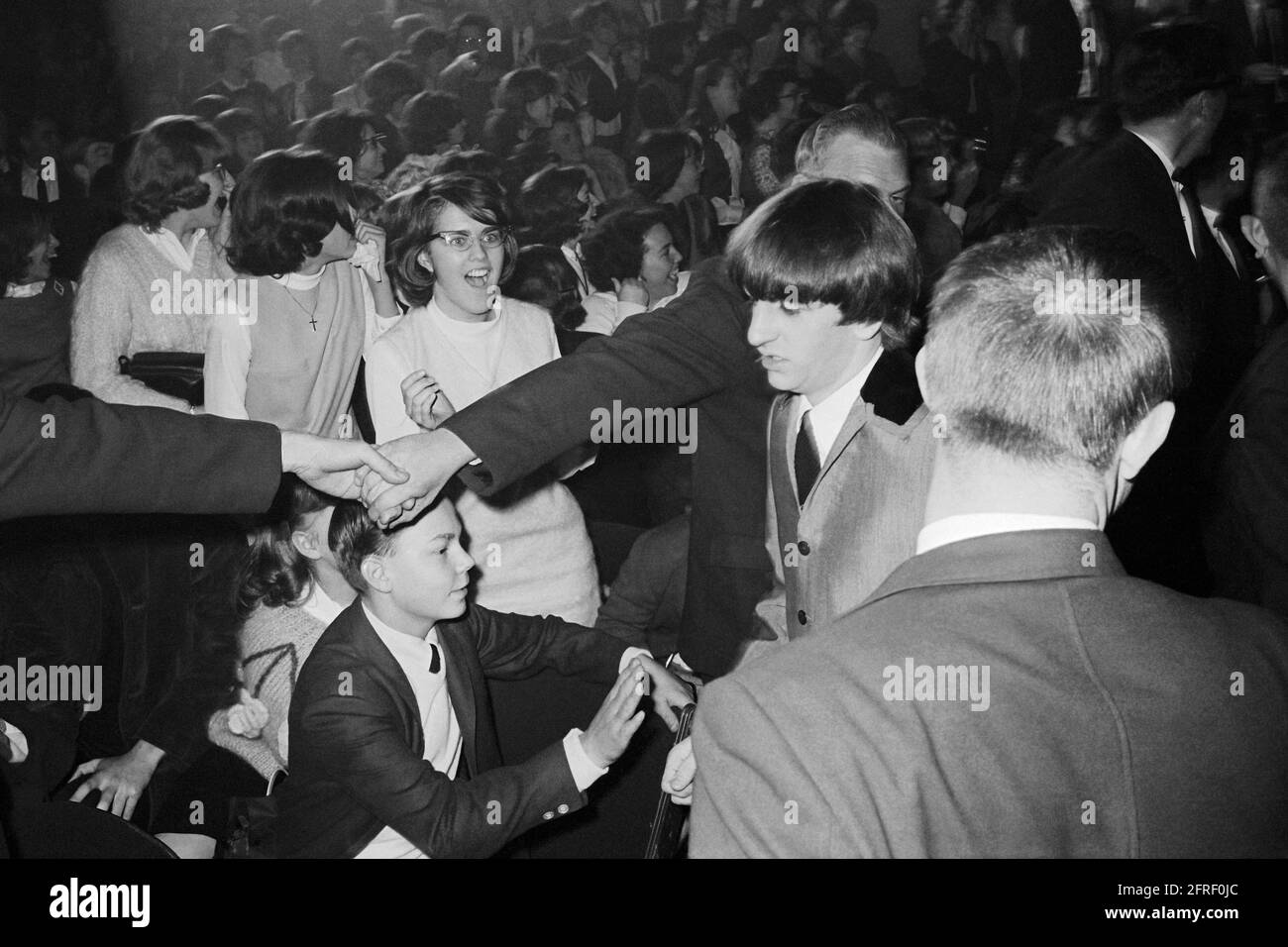 Die Polizei schließt sich den Händen, um die Fans anzubeten, während Ringo Starr am Washington Coliseum in Washington, D.C. vorbei geht, wo die Beatles am 11. Februar 1964 bei ihrem ersten amerikanischen Konzert auftrat. (USA) Stockfoto