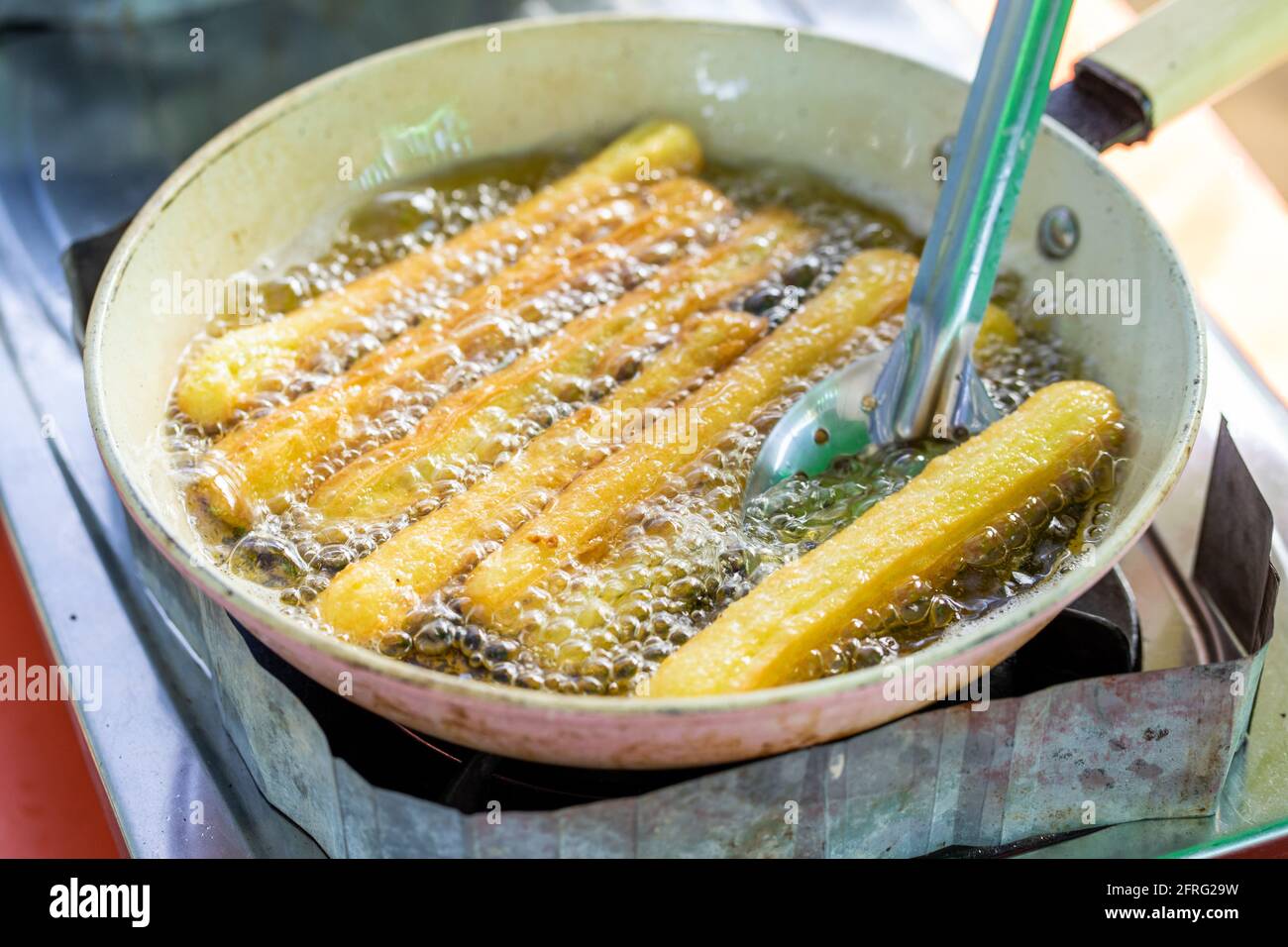 Churros werden in einer flachen Pfanne gebraten. Stockfoto