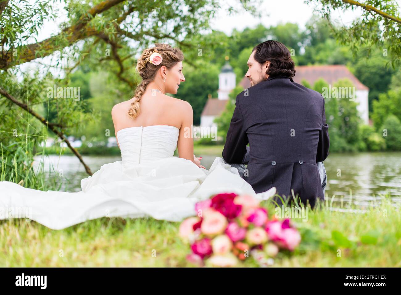 Hochzeit paar von Braut und Bräutigam sitzen auf der Wiese mit Brautstrauß hinter Ihnen, candid Shot Stockfoto