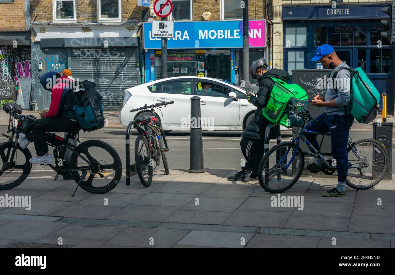 London. UK- 05.18.2021: Junge Männer arbeiten als selbstständige Reiter für Online-Lebensmittelbestellungsunternehmen, die auf ihre nächste Arbeitsbenachrichung am Telefon warten. Stockfoto