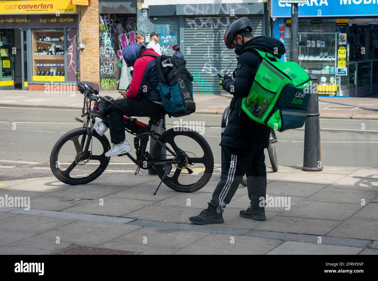London. UK- 05.18.2021: Junge Männer arbeiten als selbstständige Reiter für Online-Lebensmittelbestellungsunternehmen und warten auf ihre nächste Arbeitsbenachrichung. Stockfoto