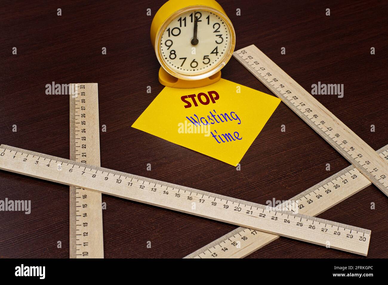 ERINNERUNG AN VERSCHWENDETE ZEIT auf dem gelben Aufkleber neben dem Alarm BEENDEN Uhr und messende Holzlineale auf dem Schreibtisch Stockfoto