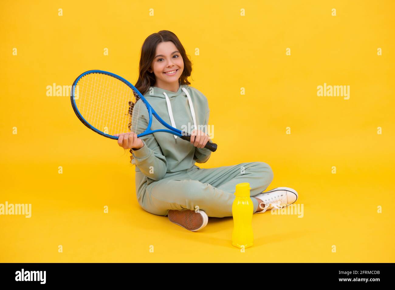 Kind sitzen mit Schläger und Wasserflasche. Kind mit Tennisschläger. Teenager-Mädchen nach dem Sporttraining. Stockfoto