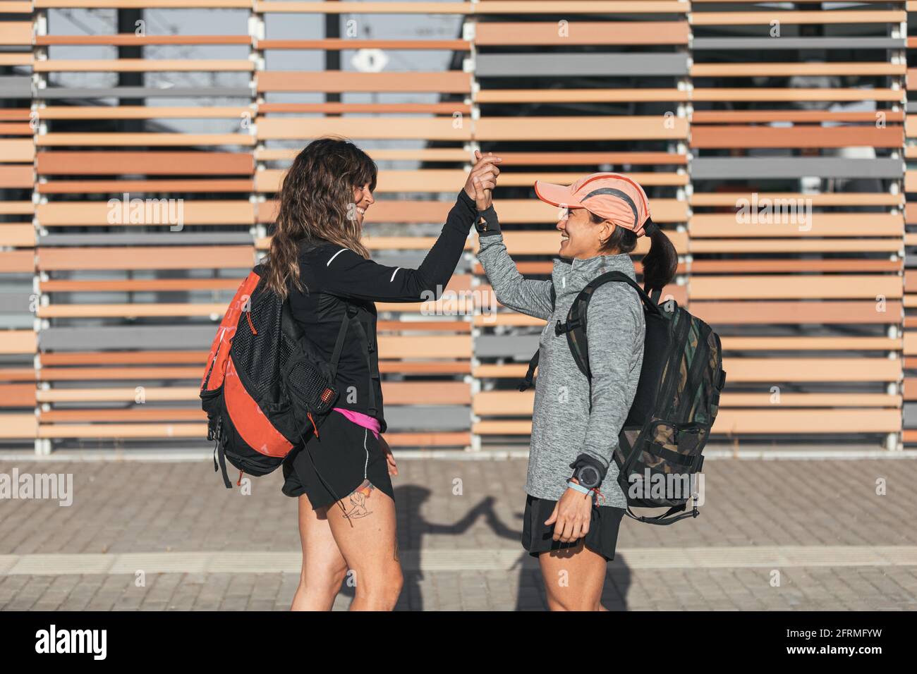 Zwei glückliche Freunde grüßen und treffen sich auf der Straße.Treffen, um zu laufen, einen Rucksack mit Sportkleidung zu tragen Stockfoto