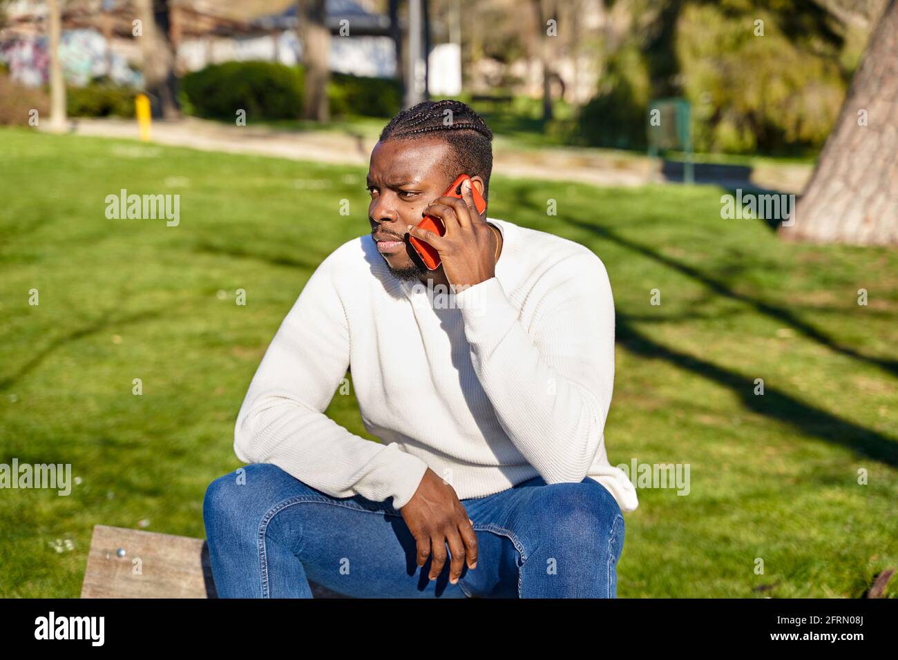 Junger afroamerikanischer Mann, der in einem Park am Handy telefoniert. Schwarzer Mann mit Zöpfen im Haar. Hochwertige Fotos Stockfoto