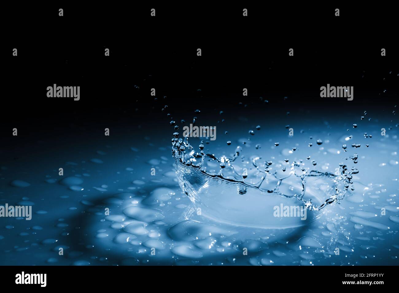 Wunderschöne Spritzkrone aus einem Tropfen Wasser, der auf eine harte Oberfläche fällt. In blauem Licht auf schwarzem Hintergrund Stockfoto