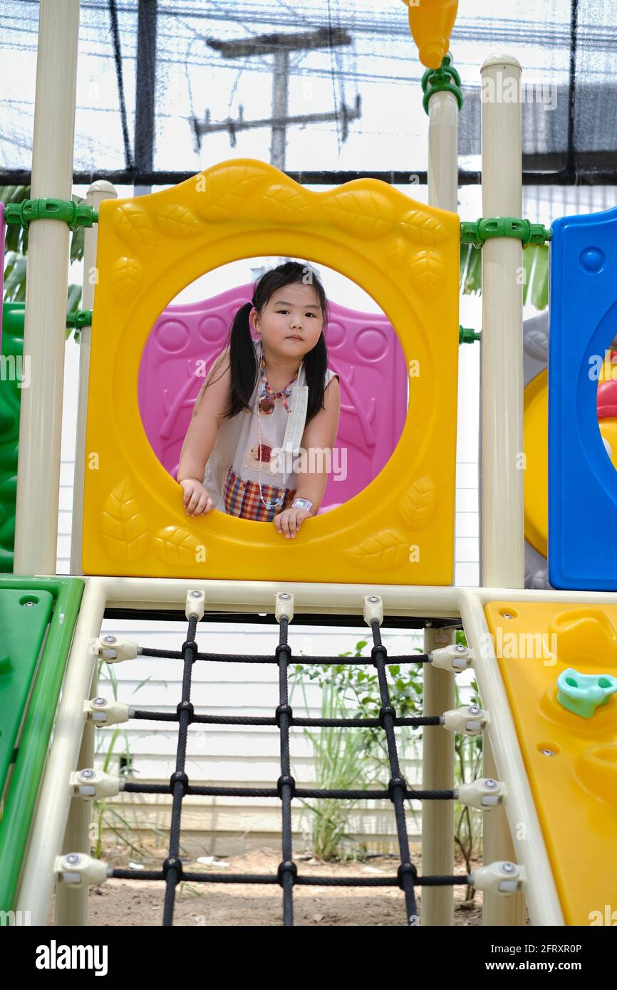 Ein süßes junges molliges asiatisches Mädchen spielt in einem bunten Kunststoff-Dschungel-Fitnessstudio, kriecht durch einen Tunnel, hat Spaß und lächelt. Stockfoto