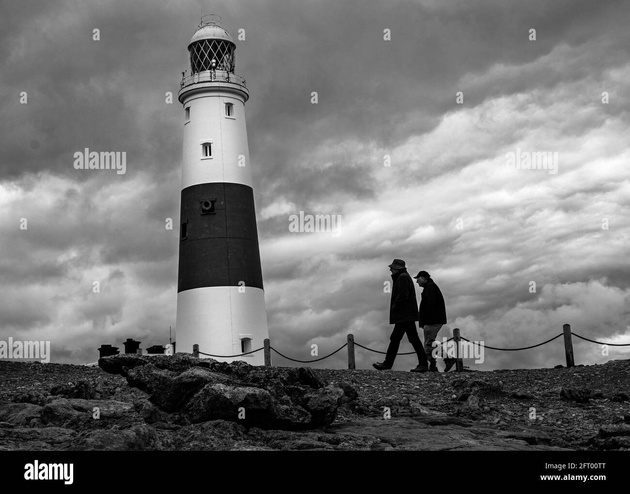 Zwei Männer wickelten sich gegen den Wind und gingen am Portland Bill Lighthouse, Dorset, Großbritannien, vorbei Stockfoto