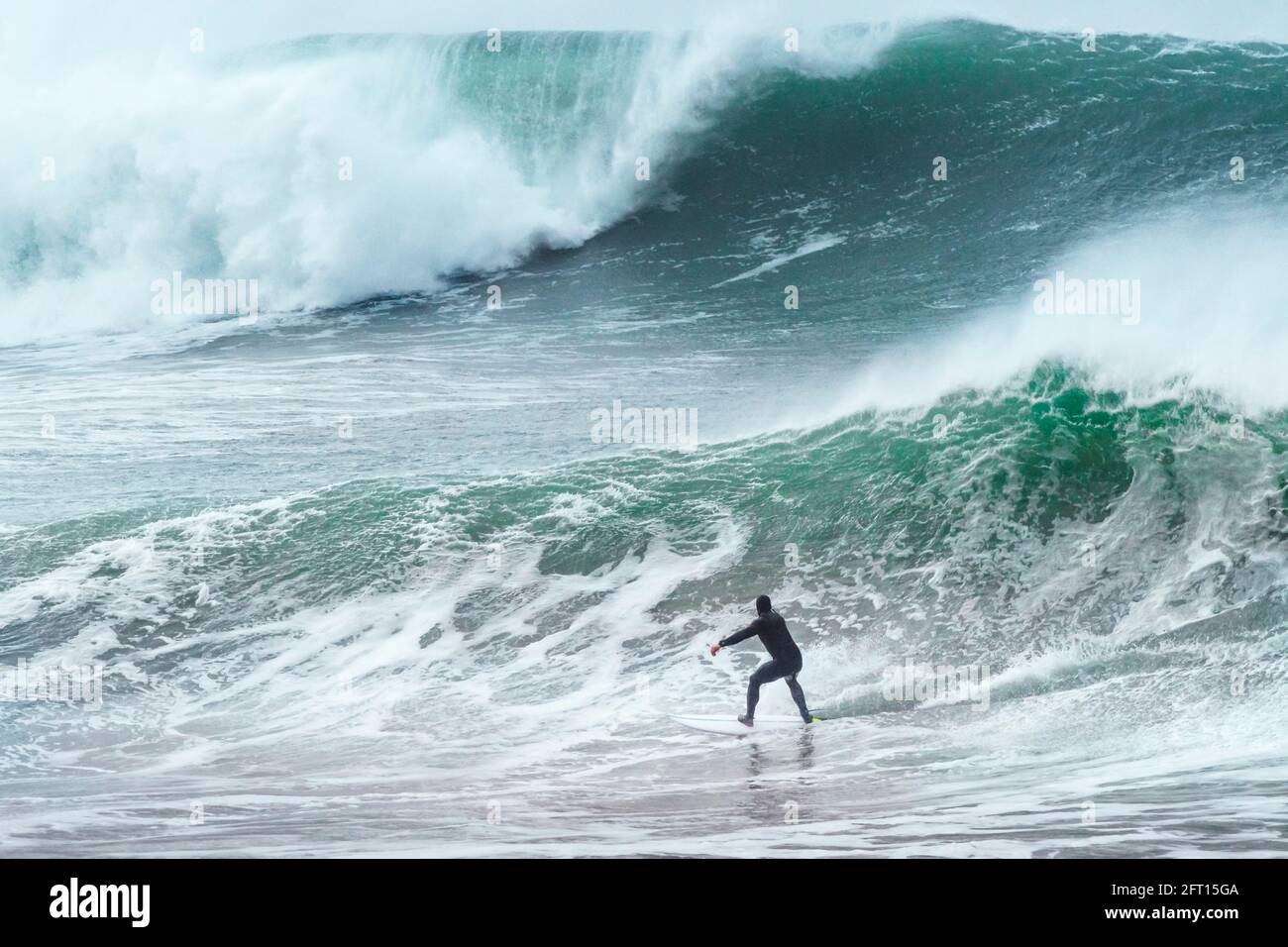 Ein Surfer, der auf riesigen Wellen über dem Cribbar Reef vor der Küste von Newquay in Cornwall reitet. Stockfoto