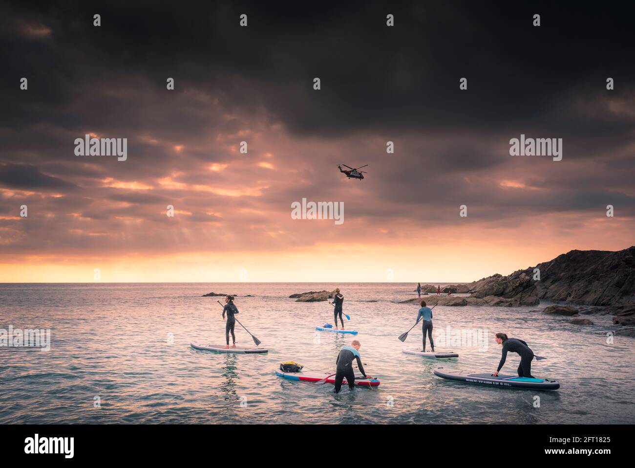 Eine Gruppe von Urlaubern paddeln auf Stand Up Paddleboards, während die Sonne über der Fistral Bay in Newquay in Cornwall untergeht. Stockfoto