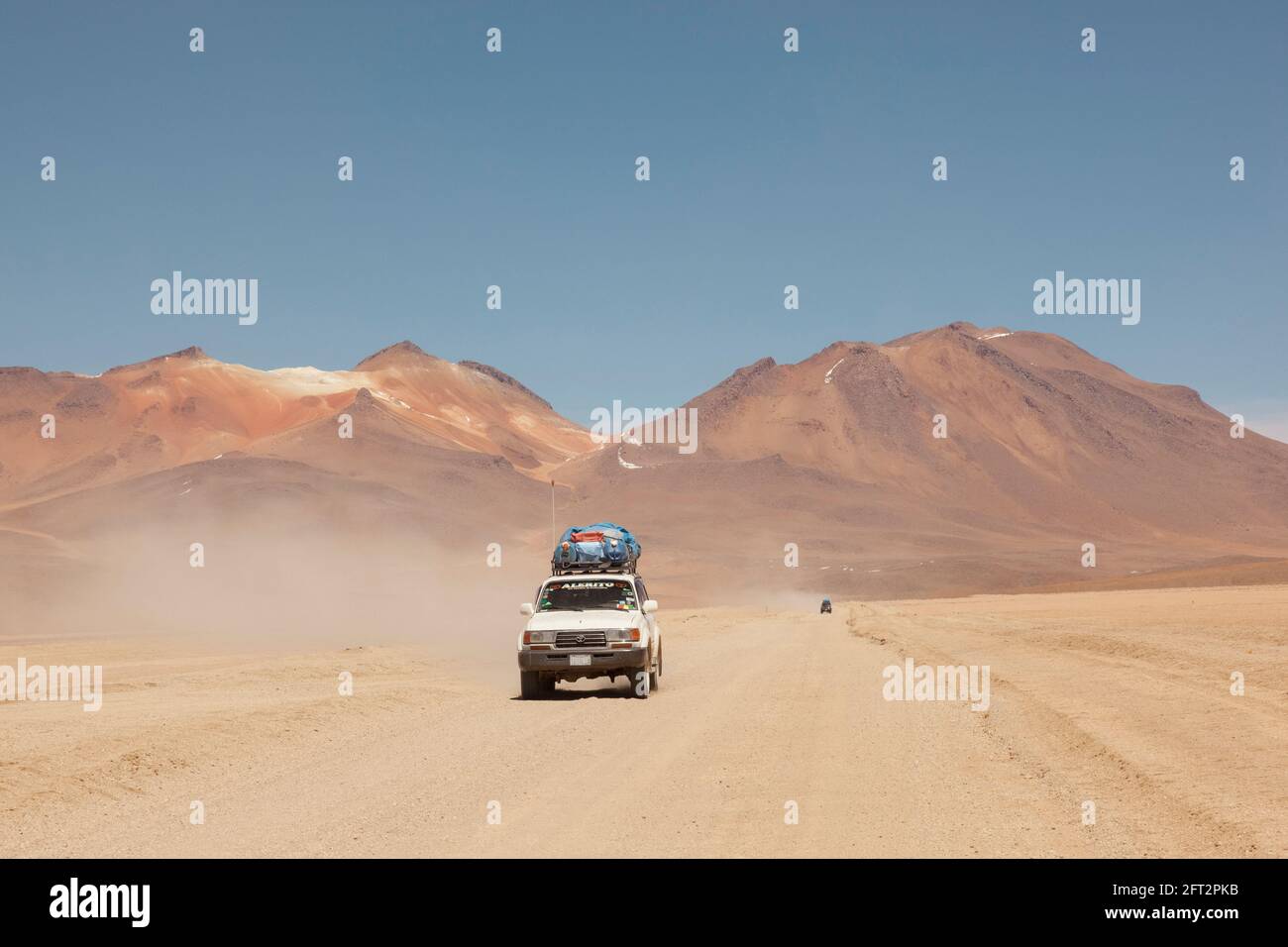 Vor dem Hintergrund von Vulkanen fährt ein Geländewagen im Geländewagen auf einer Touristensafari über Land durch die Wüstenlandschaft Boliviens. Stockfoto