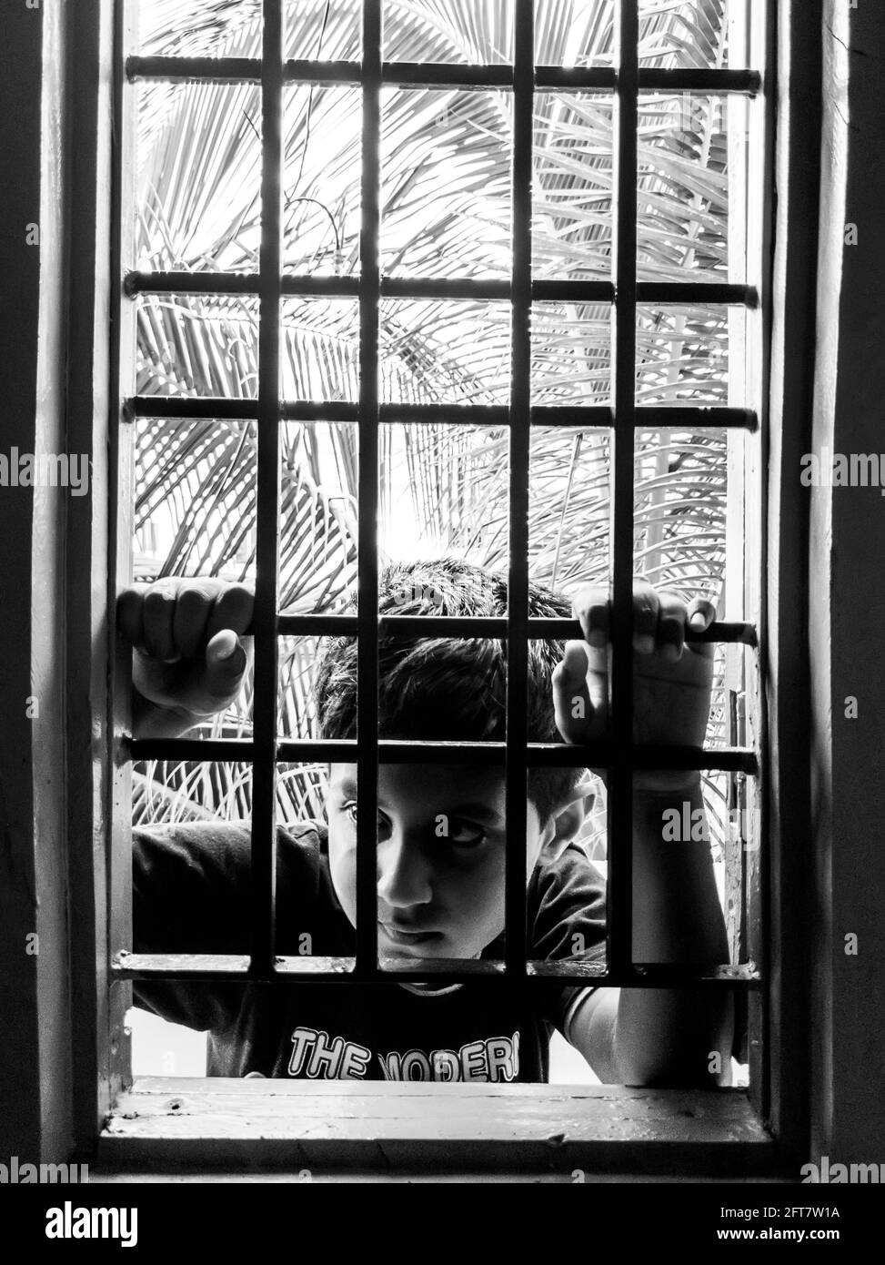 Eine Nahaufnahme eines indischen Jungen, der im monochromen vertikalen Fensterhaus-Rahmen schaute, Kalaburagi, Karnataka, Indien, Mai 10.2021 Stockfoto