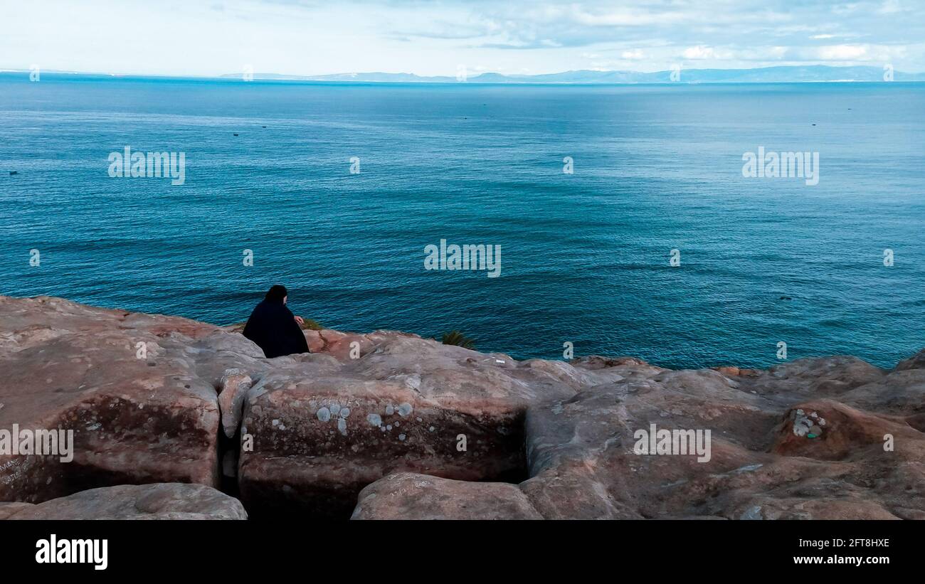 Eine Frau in islamischem Kleid sitzt allein und blickt auf das Mittelmeer. Stockfoto