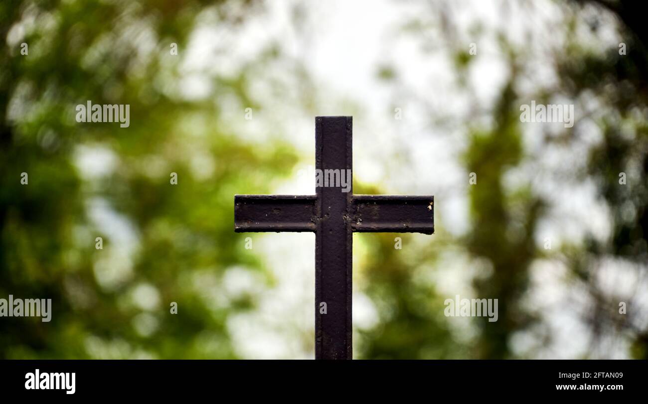 Schwarzes gusseisernes christliches Kreuz isoliert vor absichtlich verschwommenem Hintergrund Stockfoto