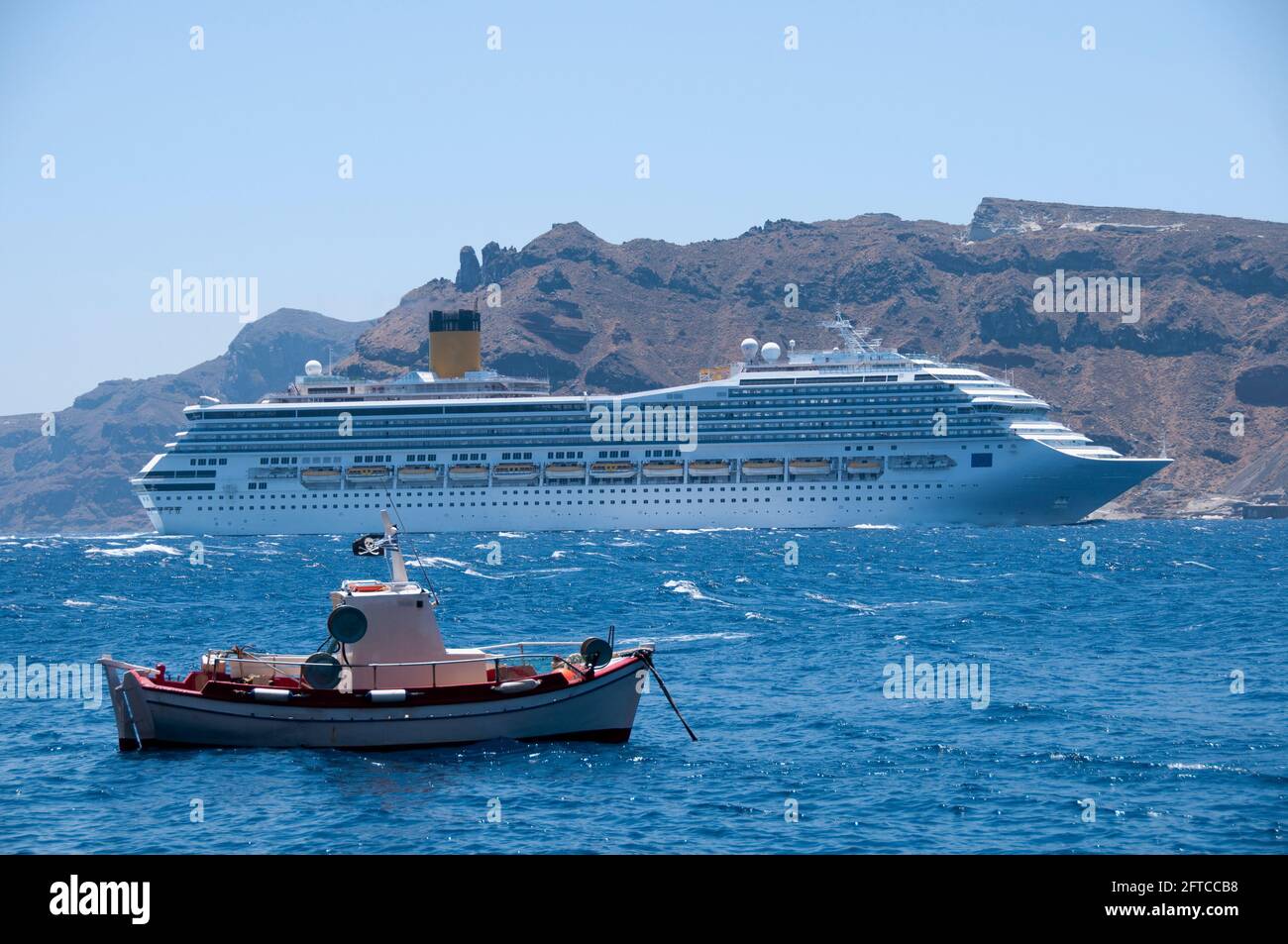 Ein Kreuzfahrt- und ein Fischerboot, das in der Caldera der Insel Santorini in Griechenland segelt. Im Hintergrund die Küste von Thirasia Stockfoto